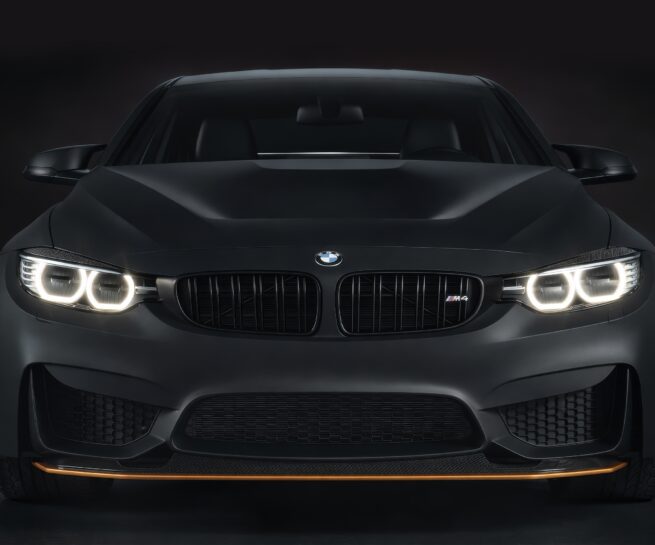 Dark automotive CGI of a black coupe with illuminated headlights in a studio environment.