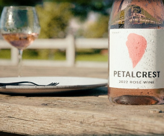 Photoreal CGI of a Petalcrest rosé wine bottle on a wooden table with glasses in the background.