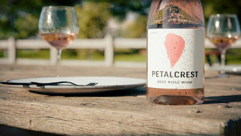 Photoreal CGI of a Petalcrest rosé wine bottle on a wooden table with glasses in the background.